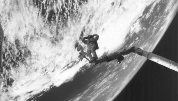In a triumphant ending to a triumphant space salvage, James “Ox” van Hoften strikes a Charles Atlas pose on the end of the shuttle’s RMS mechanical arm, seemingly hoisting the world on his shoulders (Credits: NASA).