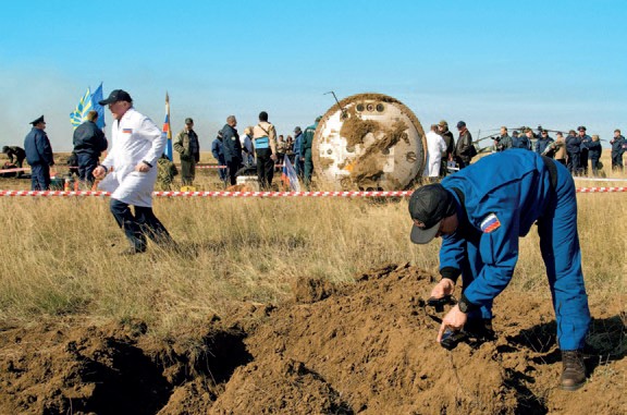 A Russian ground crew member examines the over turned soil near the Soyuz TMA-11 spacecraft after it landed (Credits: NASA).