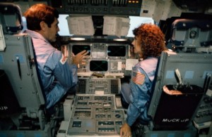 Mission 51L Commander Dick Scobee talks to schoolteacher Christa McAuliffe about the instrumentation of the shuttle’s flight deck during pre-launch training (Credits: NASA).