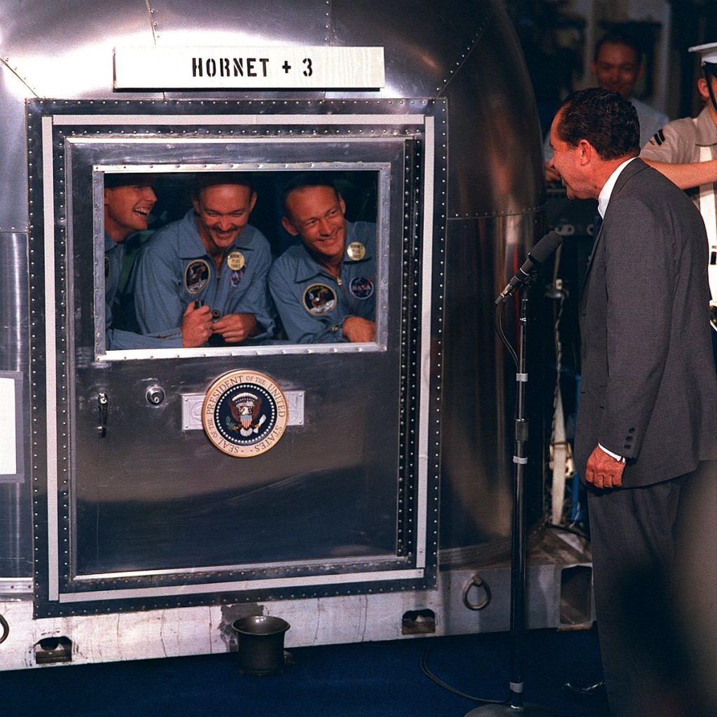 Caption: Apollo 11 astronauts Neil Armstrong, Buzz Aldrin, and Michael Collins talk with Pres. Nixon from the Mobile Quarantine Facility, an anti-contamination measure devised to prevent backward contamination from the Moon. – Credits: NASA.