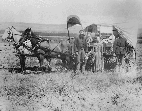 A family poses with the wagon in which they live and travel daily during their pursuit of a homestead. - Credits: NARA - ARC Identifier 518267.